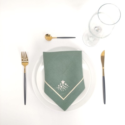 Conjunto de mesa com prato, guardanapo verde, talheres dourados e copo de vinho