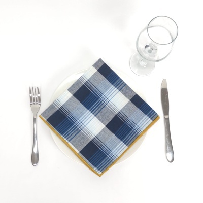 Mesa posta com guardanapo xadrez azul em prato branco, talheres e copo