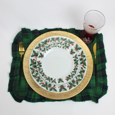 Conjunto de pratos decorados com folhas verdes e bagos vermelhos sobre base dourada, talheres douradas, copo e guardanapo verde escuro xadrez