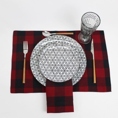 Conjunto de mesa com pratos brancos e pretos, talheres com cabos de madeira, copo gravado e base xadrez vermelha e preta