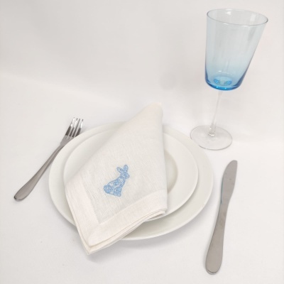 Serviço de mesa com guardanapo branco bordado, pratos brancos, talheres metálicos e copo azul