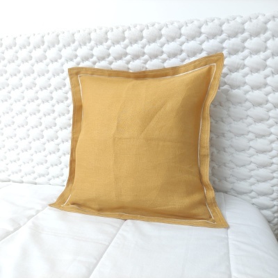 Almofada quadrada amarela mostarda sobre cama branca com colcha e cabeceira acolchoada