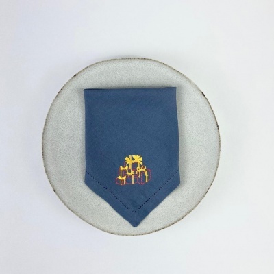 Pano azul bordado com motivos de palmeira e presentes sobre prato cinza redondo.