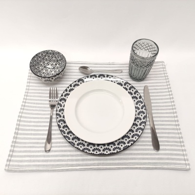Conjunto de jantar com pratos, tigela, copo e talheres sobre individual listrado