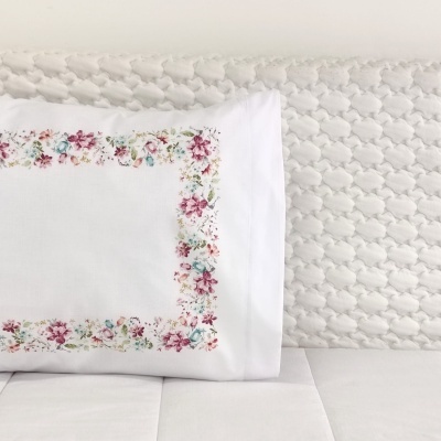 Travesseiro branco com fronha floral colorida sobre colchão e almofada brancos texturizados
