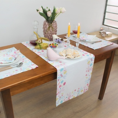 Mesa de madeira decorada para Páscoa com toalha branca com flores, velas, vaso com flores e decorações de coelho