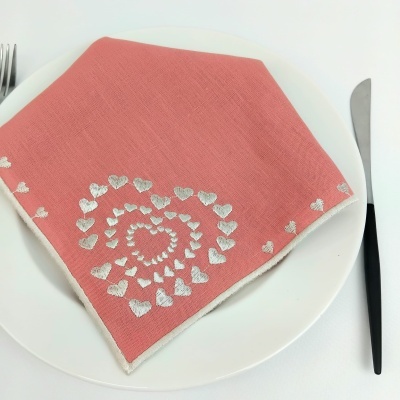 Guardanapo cor de coral com padrão de corações brancos, prato branco, talheres