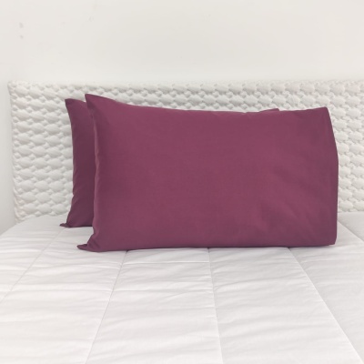 Duas almofadas bordô sobre cama branca com cabeceira texturada