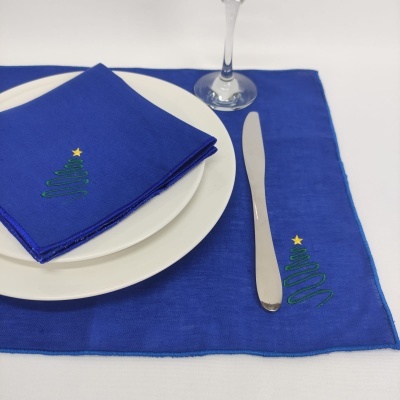 Guardanapo e individual azuis com bordado de árvore de Natal verde e estrela amarela, prato branco e faca