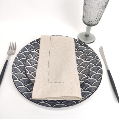 Prato cerâmico azul e branco com padrão, guardanapo bege, talheres pretos e copo cinza texturizado