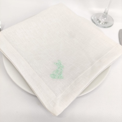 Guardanapo branco com bordado de coelho verde sobre prato