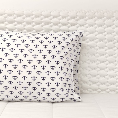 Almofada branca com padrão de âncoras pretas num sofá branco com textura acolchoada.