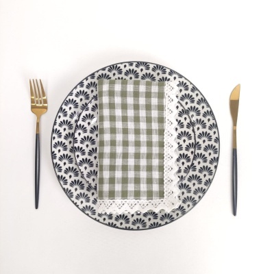 Conjunto de pratos cerâmicos com padrão preto, guardanapo xadrez verde e branco, talheres pretos com dourado