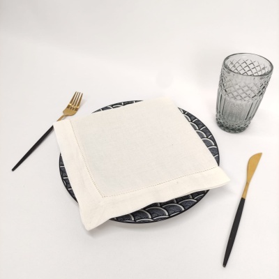 Talheres dourados com cabos pretos, prato azul escuro com padrão geométrico, guardanapo branco e copo de vidro texturizado sobre fundo branco