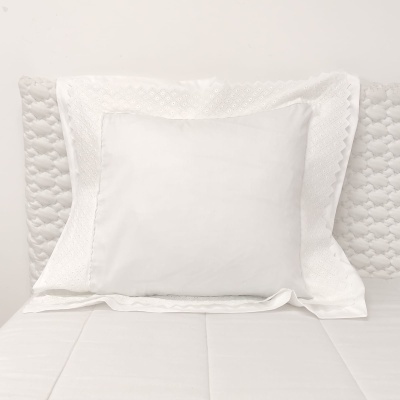 Almofada branca com fronhas bordadas em cama branca e cabeceira acolchoada.