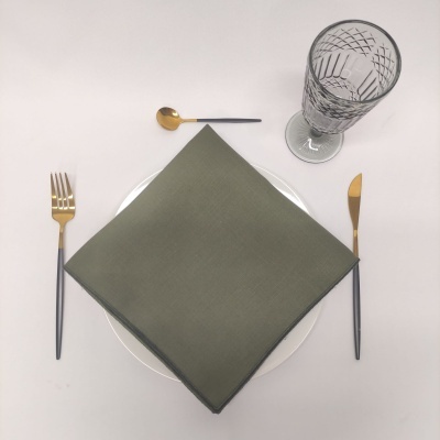 Conjunto de talheres dourados e pretos junto a guardanapo verde e copo de vidro gravado sobre mesa branca