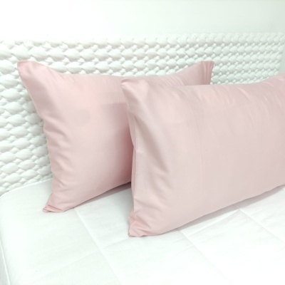 Duas almofadas cor-de-rosa sobre cama branca com cabeceira texturizada.