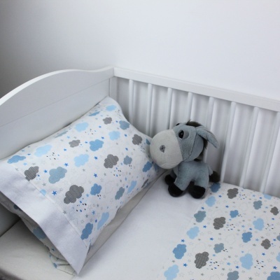 Berço branco com lençóis e fronha decorados com padrão de nuvens azul e cinzento e peluche
