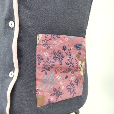 Peça têxtil azul escura com bolso cor-de-rosa decorado com padrão floral e guaxinim