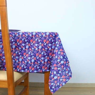 Toalha de mesa azul escura com padrão floral colorido sobre mesa de madeira com cadeira ao lado