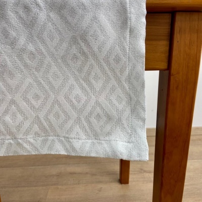 Toalha de mesa branca com padrão geométrico em relevo pendurada numa mesa de madeira clara