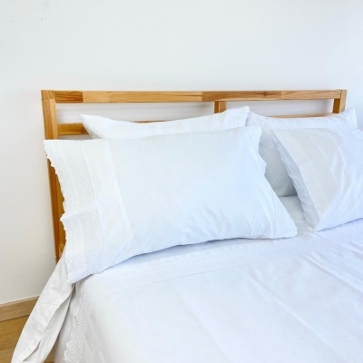 Cama com roupa de cama branca e cabeceira de madeira clara