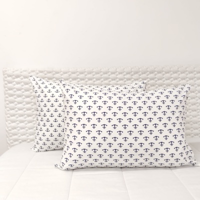 Almofadas brancas com padrão de âncoras azuis sobre cama branca com cabeceira acolchoada