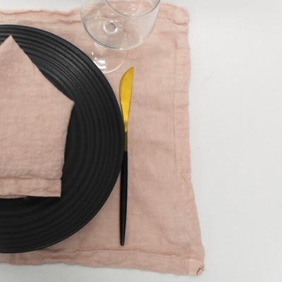 Conjunto de mesa com prato preto, guardanapo e toalhete cor de rosa claro, faca dourada e preta, copo transparente.