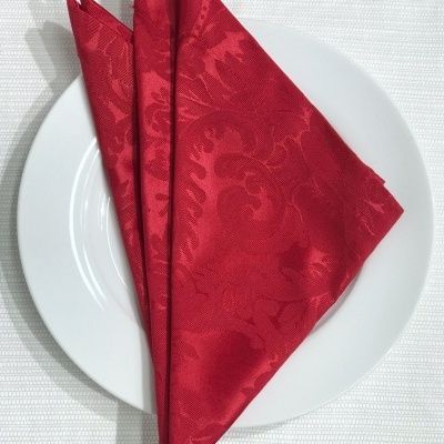 Guardanapo vermelho dobrado sobre prato branco, em toalha branca texturada