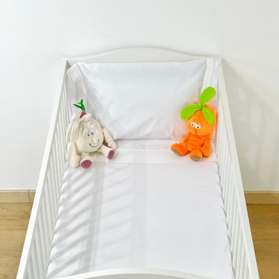 Berço branco com roupa de cama branca e dois peluches, um de cebola e outro de cenoura