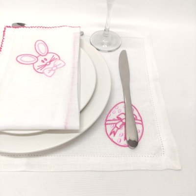 Jogo americano e guardanapo brancos com bordados cor-de-rosa de coelho e ovo, prato, faca e copo de vinho