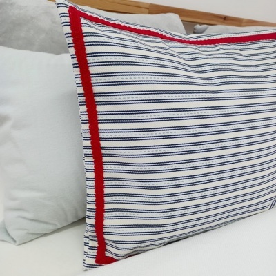 Almofada às riscas azuis e brancas com borda vermelha numa cama com almofadas brancas