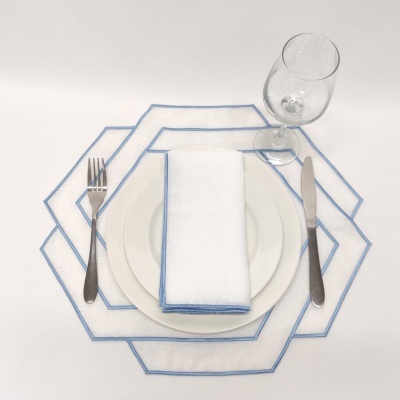 Conjunto de mesa com pratos brancos, guardanapo branco com borda azul, talheres metálicos e copo de vidro