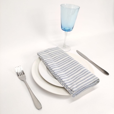 Mesa posta com prato branco, talheres prateados, guardanapo riscado e copo azul