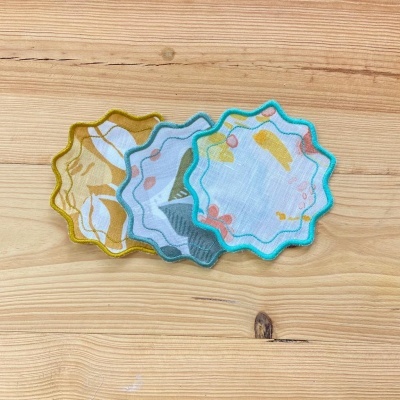 Três apliques têxteis em forma de flor com bordas coloridas em madeira clara