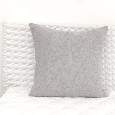 Almofada cinza com padrão floral sobre cama branca acolchoada