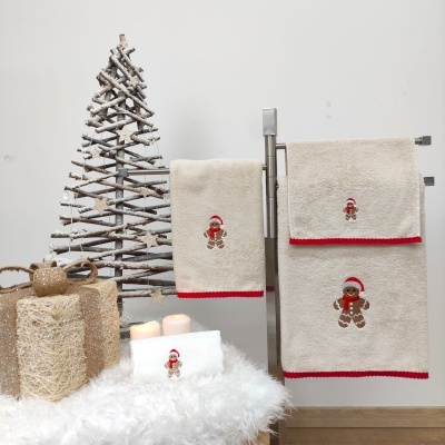 Toalhas de algodão bege com bordado natalício de biscoito de gengibre ao lado de árvore decorativa branca e presentes