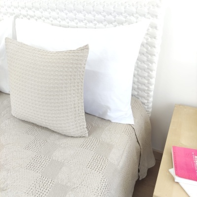 Cama com colcha e almofadas bege e brancas ao lado de mesa com livros