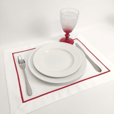 Conjunto de pratos, talheres, conjunto americano branco com borda vermelha e copo de vidro com haste vermelha.