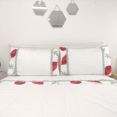Conjunto de roupa de cama branca com flores vermelhas e folhas verdes colocado numa cama.