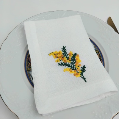 Guardanapo branco bordado com flores amarelas sobre prato decorativo