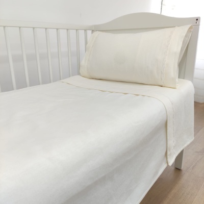 Cama branca de solteiro com roupa de cama creme e detalhes rendados