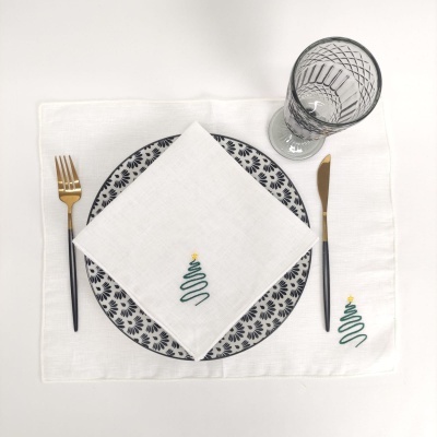 Conjunto de guardanapo e individual com bordado de árvore de Natal, prato com padrão azul, talheres dourados e copo de vidro