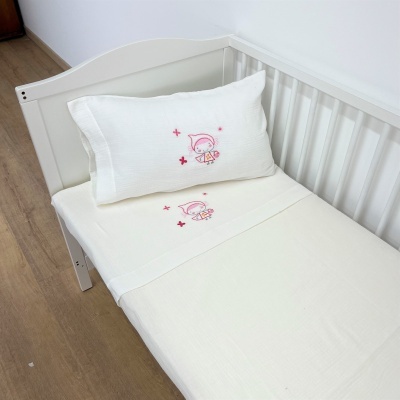 Conjunto de roupa de cama branca para berço com bordado rosa de menina e flores em berço branco.