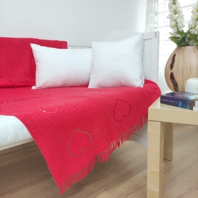 Manta vermelha com corações num sofá branco com almofadas brancas e decoração ao lado.