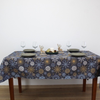 Mesa de madeira com toalha azul escura com flocos de neve e decoração de Natal, com pratos cinzentos e copos.