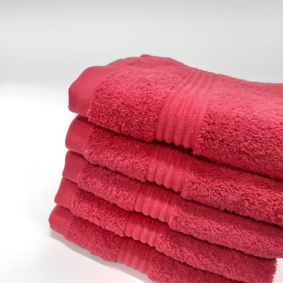 Quatro toalhas de banho rosa empilhadas com faixa riscada em fundo branco.