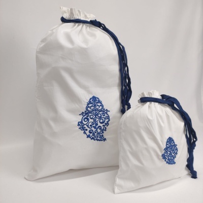 Dois sacos de tecido branco com cordão azul e padrão azul ornamental.
