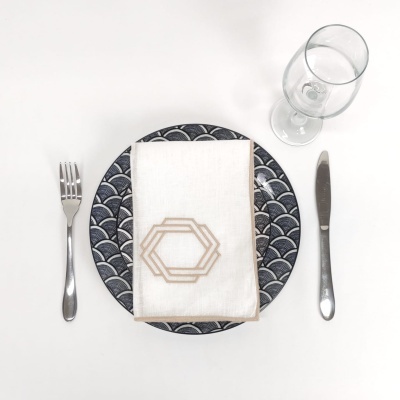 Conjunto de talheres em metal inoxidável, prato com padrão geométrico, guardanapo branco com design, e copo de vidro vazio