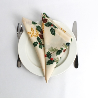 Guardanapo natalício tecido com folhas verdes e frutos vermelhos no prato branco com talheres.